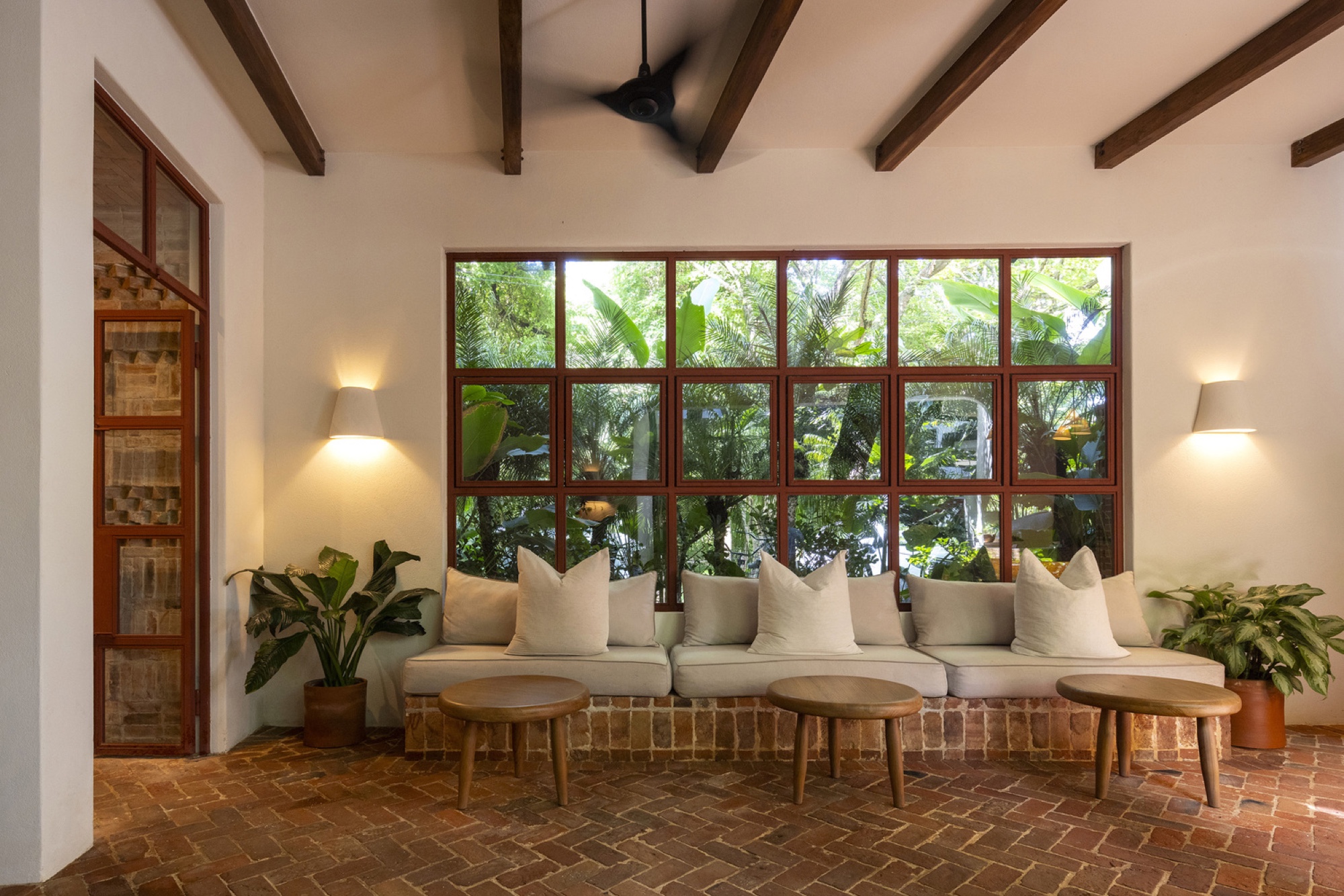 Salon lumineux à la grande verrière, banquette et sol en terre cuite, ouvert sur la végétation