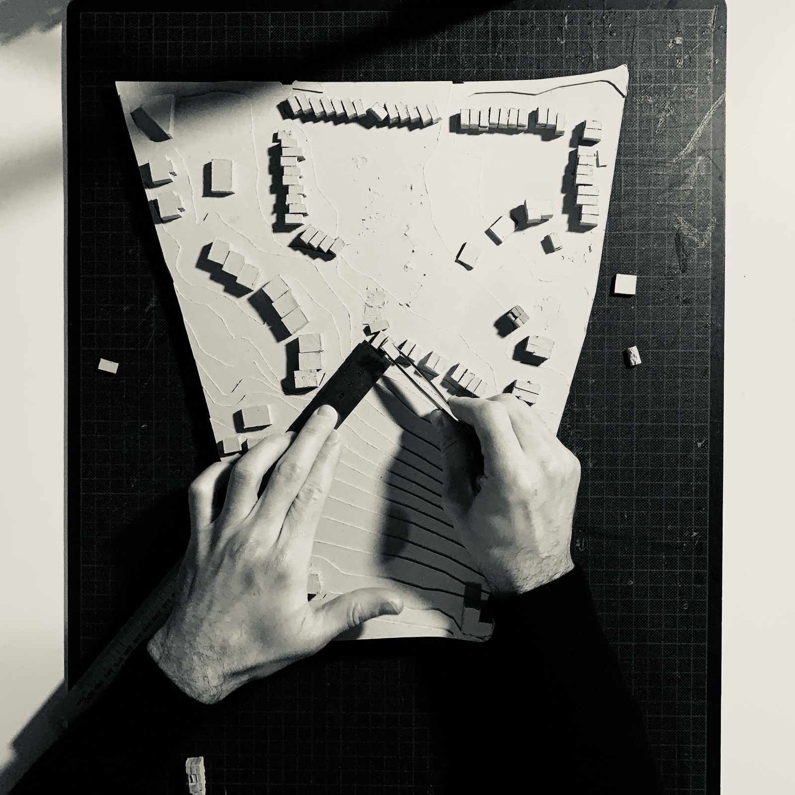Mains travaillant sur une maquette de site, réglant l'implantation des volumes à la pincette